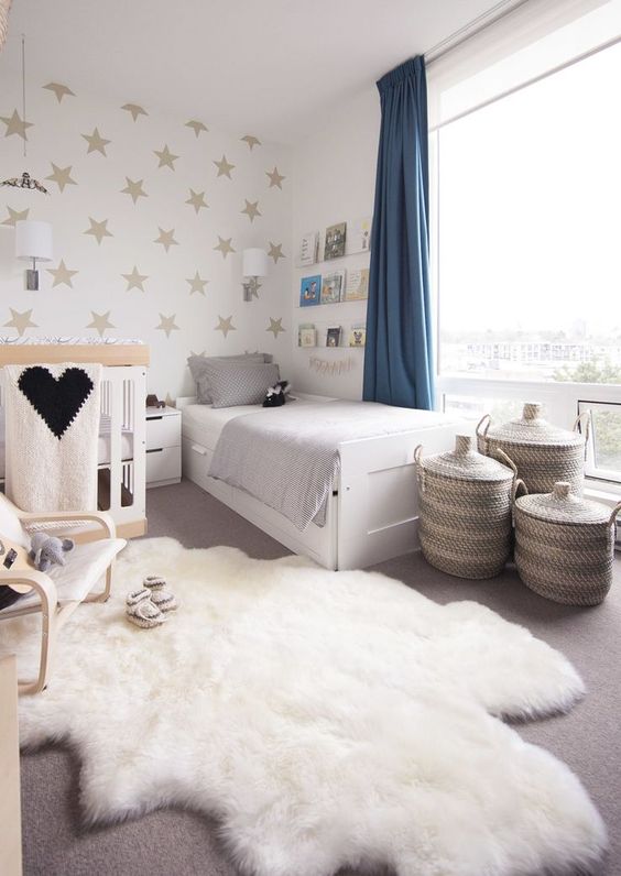 a soothing neutral shared room with a star print wall, some neutral furniture and cozy layered rugs