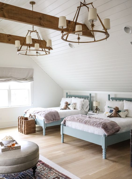 a stylish and cool attic shared girls' bedroom with blue beds, a grey pouf, a basket for storage and vintage brass chandeliers