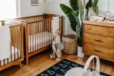 a stylish mid-century modern nursery with rich-stained furniture, a basket, a statement plant and a cool printed rug