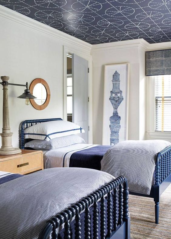 a stylish navy and white traditional shared teen bedroom with blue beds, wooden furniture and a printed ceiling