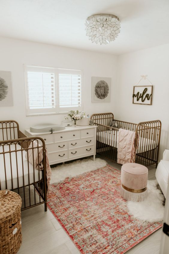 a stylish shared nursery with a vintage feel, with metal cribs, neutral furniture, a floral chandelier and printed rug