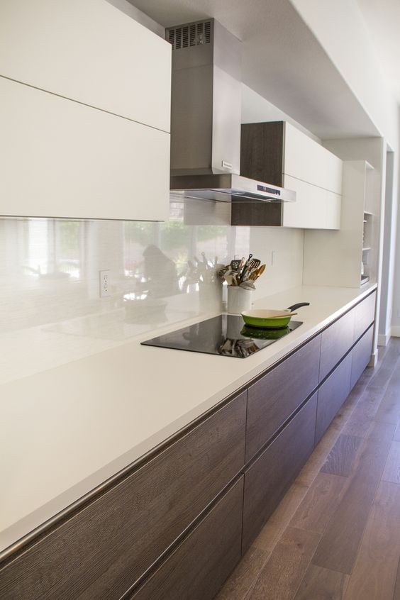 a two-tone minimalist kitchen with sleek white and dark-stained cabinets, white stone countertops and a white glas sbacksplash is chic