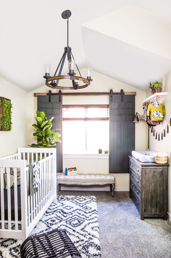 a unique farmhouse nursery with sliding shutters of vintage doors, a white crub, printed layered rugs and a vintage chandelier