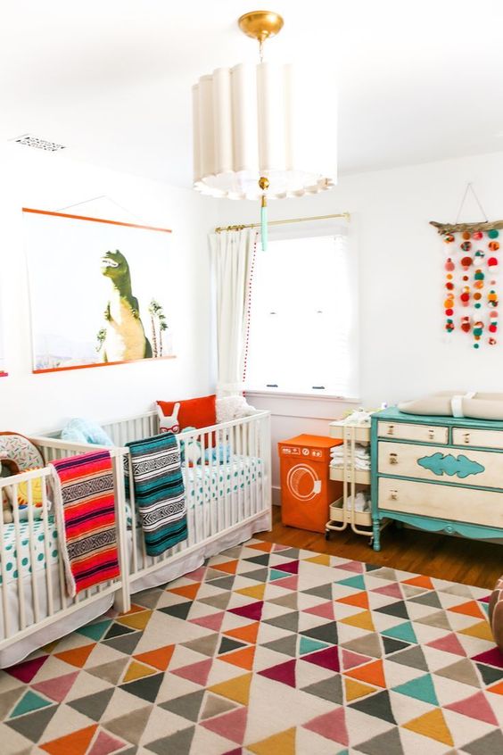 a vibrant twin nursery with colorful linens and bright furniture, a colorful mobile and an artwork