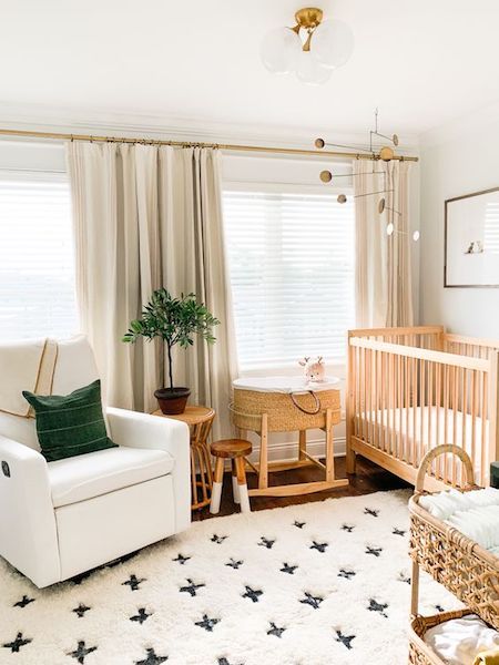 a welcoming gender neutral nursery with wooden and white furniture, a printed rug, baskets and a green pillow