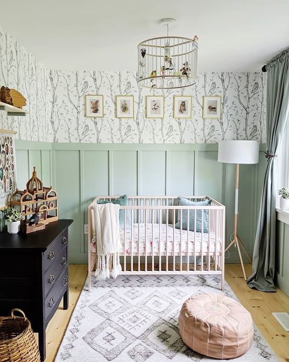 a welcoming modern nursery with green paneling, a black sideboard, a blush crib and a leather ottoman