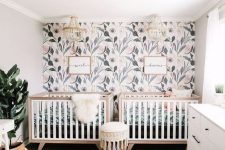 a welcoming neutral nursery with a botanical accent wall, neutral furniture, a potted plant and beaded chandeliers for decor