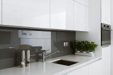 a white minimalist kitchen with white stone countertops, a grey glass backsplash plus stainless steel appliances is wow