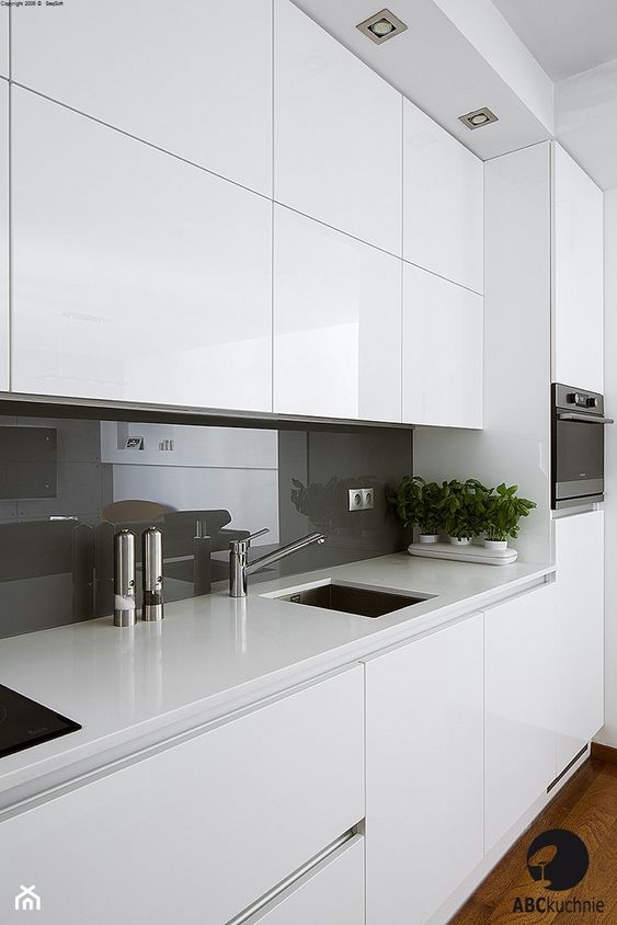 a white minimalist kitchen with white stone countertops, a grey glass backsplash plus stainless steel appliances is wow