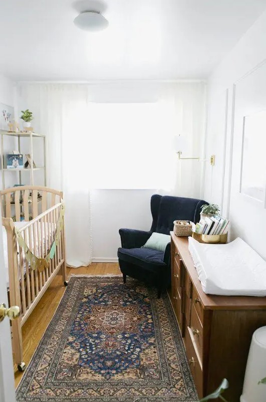 a white nursery is filled with a navy velvet chair, a printed rug and a brown wooden dresser