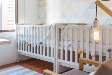 an airy and bright shared nursery with a geometric accent wall, hot air balloons and garlands and neutral furniture