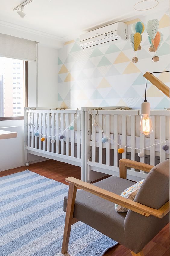an airy and bright shared nursery with a geometric accent wall, hot air balloons and garlands and neutral furniture