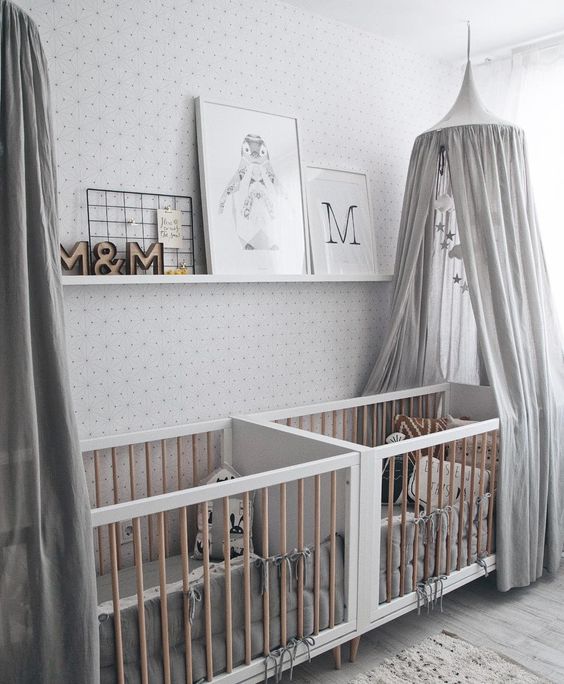 an all-neutral nursery with printed walls, white and stained furniture, grey canopies, a ledge with artworks and printed bedding