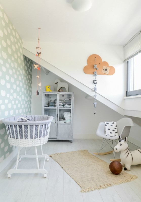 an attic Scandinavian nursery with a whitewashed wardrobe, a crib, a corcher chair, some art and a rug is fresh and ethereal