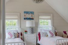 an attic shared girls’ bedroom with white beds and a nightstand, a pendant lamp, a colorful printed rug and pillows is a lovely idea
