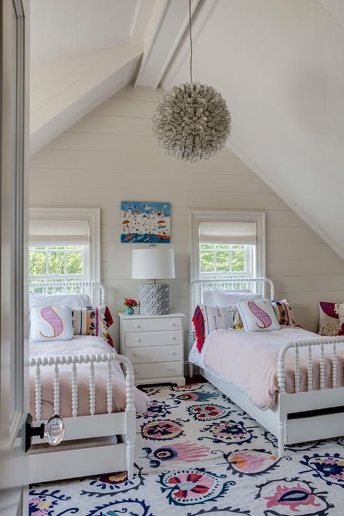 an attic shared girls' bedroom with white beds and a nightstand, a pendant lamp, a colorful printed rug and pillows is a lovely idea