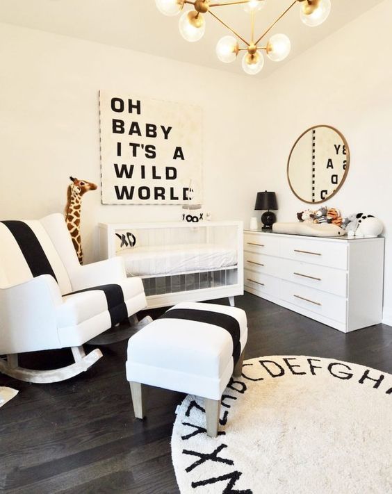 an elegant and refined monochromatic nursery with an acrylic crib, black and white art, a rug and a bold rocker