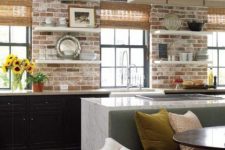 a black kitchen with lower cabinets and open shelves, brick walls as a backsplash, a white kitchen island and a pendant lamp