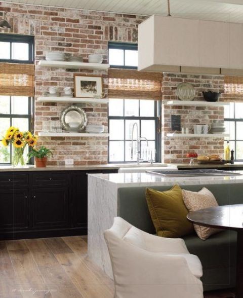 a black kitchen with lower cabinets and open shelves, brick walls as a backsplash, a white kitchen island and a pendant lamp