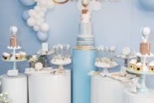 a blue and white pedestal dessert table with a hot air balloon backdrop, a balloon garland and lots of cute desserts