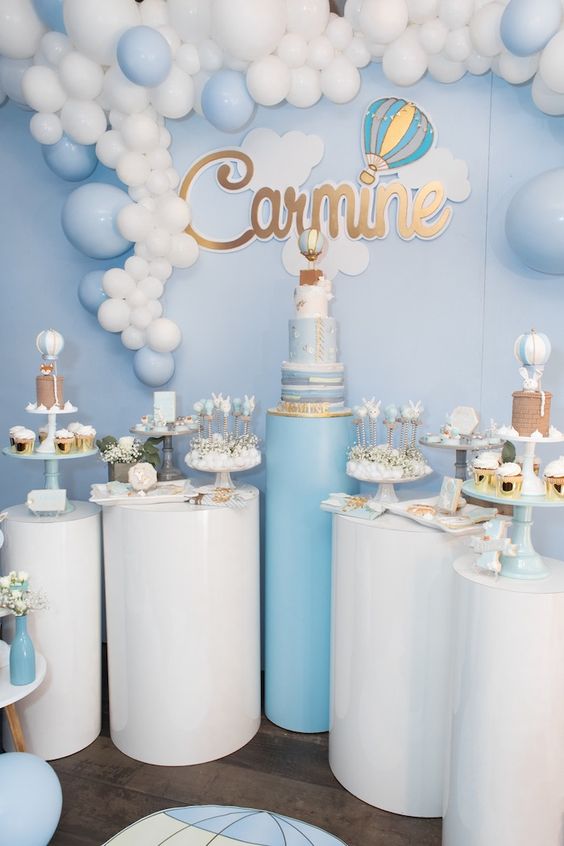 a blue and white pedestal dessert table with a hot air balloon backdrop, a balloon garland and lots of cute desserts