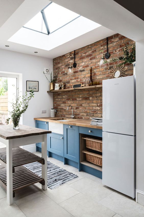 a blue farmhouse kitchen with butcherblock countertops, a red brick backsplash, a kitchen island with tiered shelves and lots of natural light