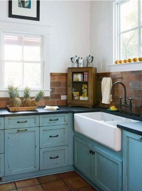 a blue shabby chic blue kitchen with dark countertops and a red faux brick backsplash for a texture