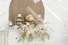 a delicate fall dessert table with a vintage sideboard, lots of painted pumpkins, a pink floral arrangement and a pink doily garland