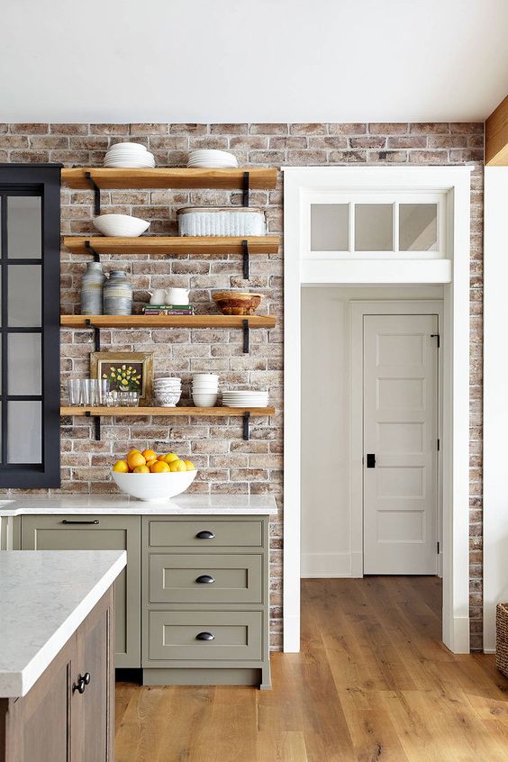 a grey shaker style kitchen with white stone countertops, open shelves, a stained kitchen island and a red brick wall as a backsplash
