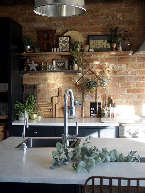a navy kitchen with white stone countertops, open shelves, greenery and pendant lamps plus a red brick wall as a backsplash