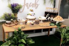 a neutral dessert table with tropical leaves and plants, with white and purple blooms and lots of sweets