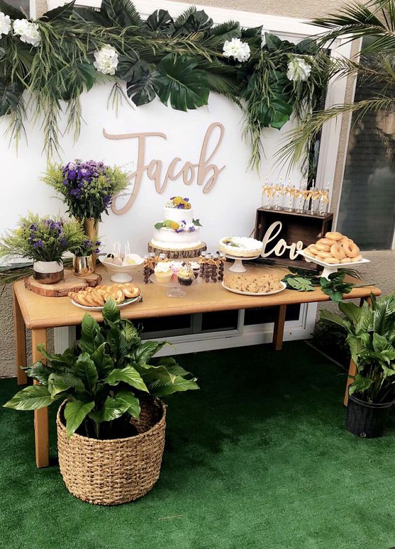 a neutral dessert table with tropical leaves and plants, with white and purple blooms and lots of sweets