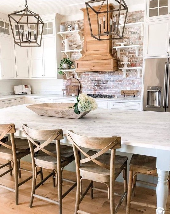 a neutral farmhouse kitchen with white cabinets, a red brick backsplash and some metal lanterns over the island