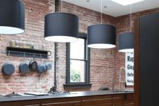 a red brick wall and rich stained wooden cabinets for a masculine feel in the kitchen and black pendant lamps over it