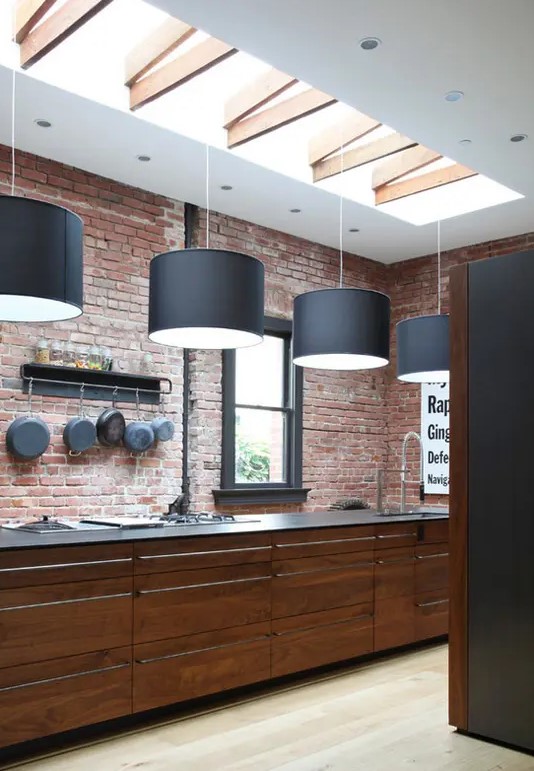 a red brick wall and rich stained wooden cabinets for a masculine feel in the kitchen and black pendant lamps over it