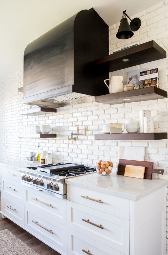 a vintage kitchen with white cabinets, copper hardware and a white faux brick wall that makes the hood stand out