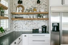 a white farmhouse kitchen with shaker cabinets, black stone countertops, white shelves, a whitewashed red brick backsplash