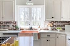 a white farmhouse kitchen with shaker style cabinets, a red brick backsplash, white stone countertops and a kitchen island with a stained countertop