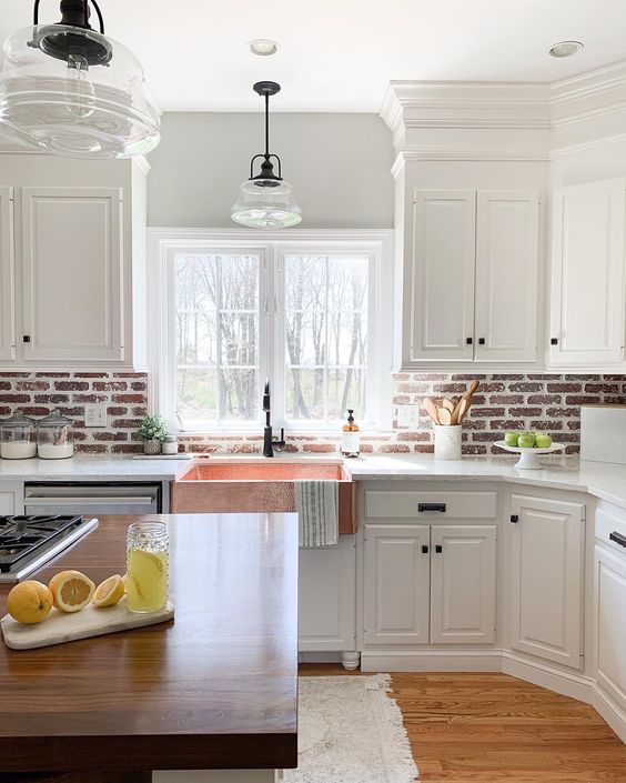 a white farmhouse kitchen with shaker style cabinets, a red brick backsplash, white stone countertops and a kitchen island with a stained countertop