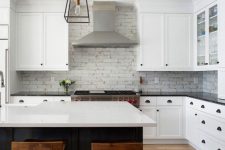 a white farmhouse kitchen with shaker style cabinets, a white brick backsplash, glass cabinets and stainless steel appliances