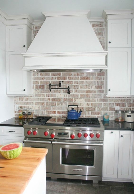 a white farmhouse kitchen with shaker style cabinets, a whitewashed red brick backsplash, stainless steel appliances and black handles