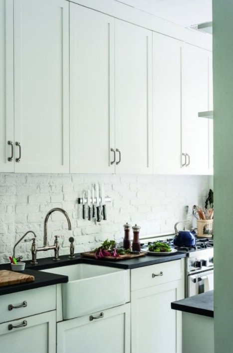an all-white kitchen with a white brick backsplash for a textural feel, black countertops and dark metal handles