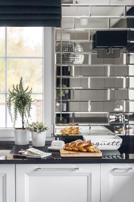 One of the walls is clad with large mirror tiles that add glam chic and make the kitchen look bigger