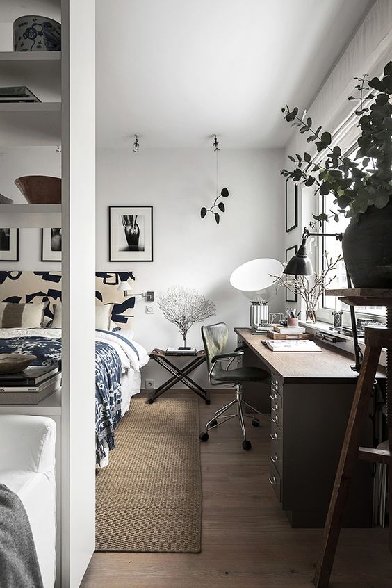 a Scandinavian bedroom with a large bed and printed bedding, a large desk, a black chair, a nightstand and cool artwork