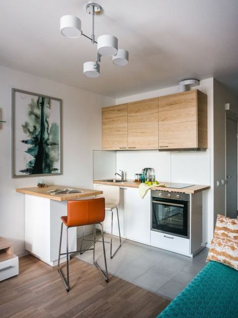 a Scandinavian kitchen with sleek white and MDF cabinets, a tiny kitchen island, a tile floor with a border and a laminate floor in the living room zone
