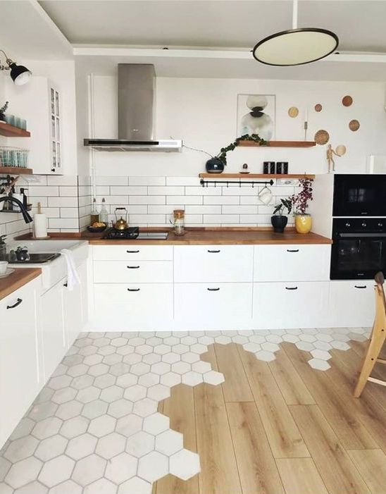 a Scandinavian kitchen with white cabinets, butcherblock countertops, a subway tile backsplash and a cool floor transition from hex tiles to laminate