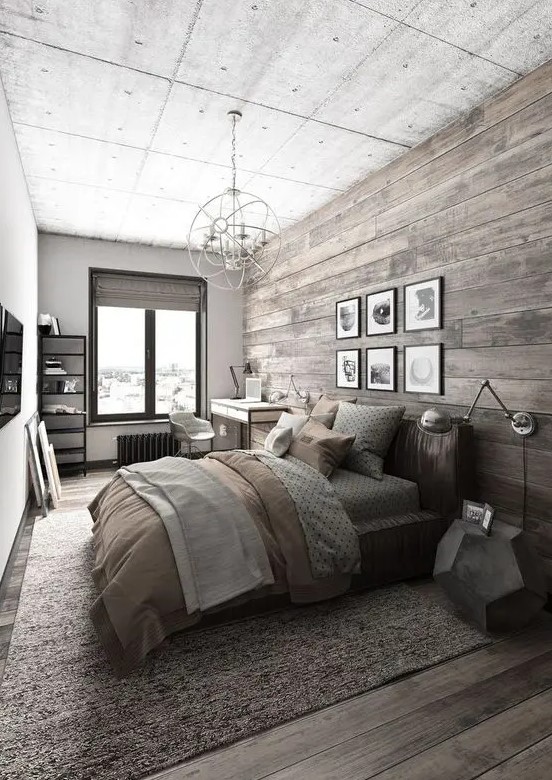 a bedroom with a wall and floor of reclaimed wood, a bed with grey and beige bedding, a desk and a chair at the window and a shelving unit