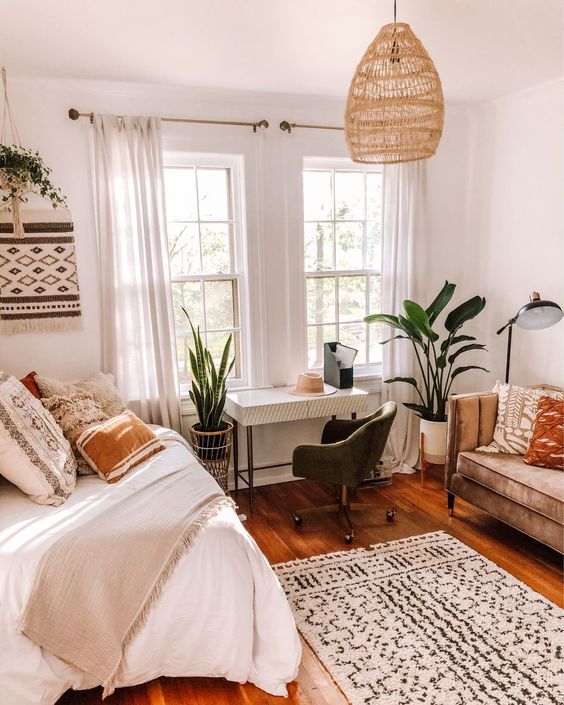 a boho bedroom with a bed and neutral bedding, a sofa, a small desk and a black chair, printed textiles, a pendant lamp