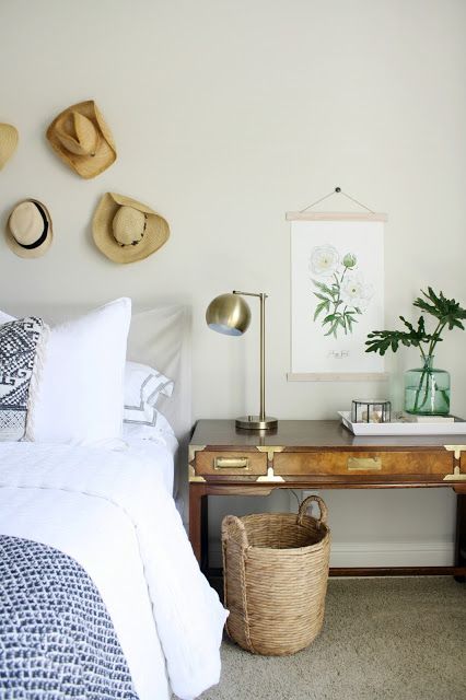 a boho bedroom with grey walls, a grey bed with printed bedding, a stained desk, a basket and a hat gallery wall
