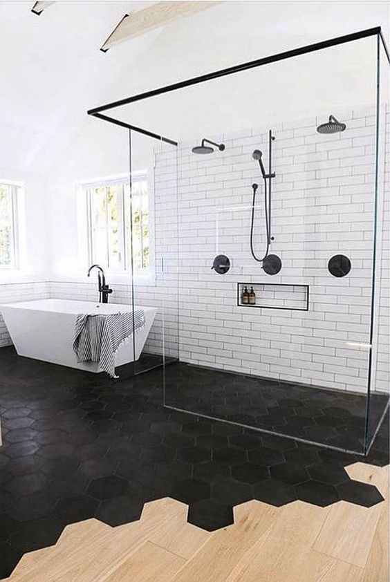 a bold and contrasting modern bathroom with a floor transition from black hex tiles to laminate, a shower space and a bathtub